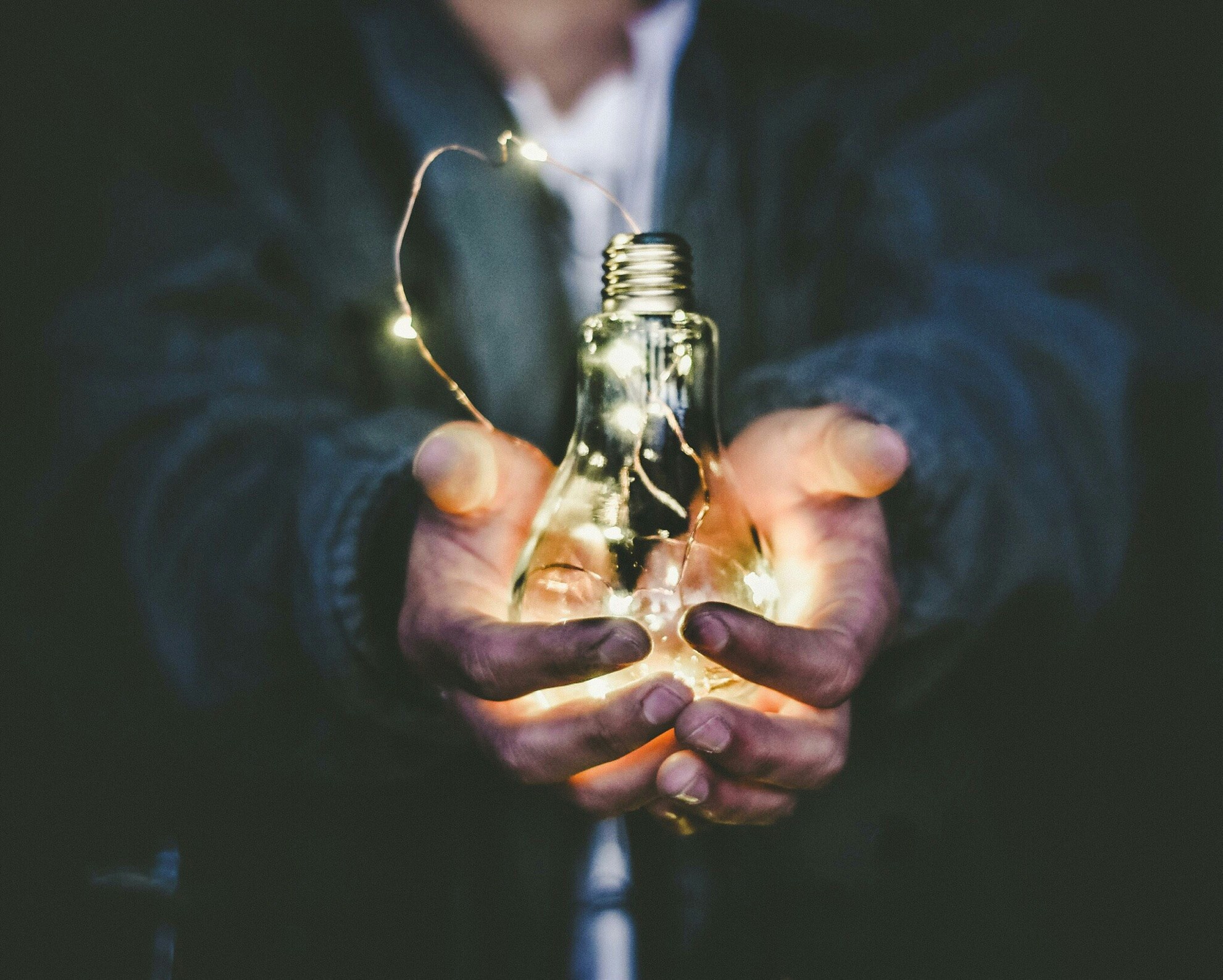 Persons hands holding lightbulb containing led light string signifying a new idea